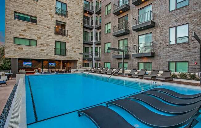 a swimming pool with chaise lounge chairs in front of an apartment building