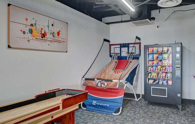 A room with a pool table, a basketball hoop, and a vending machine.