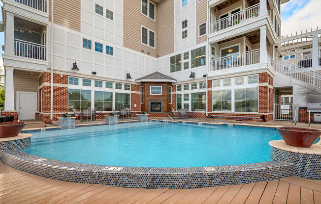 A large outdoor pool surrounded by a wooden deck and a building with balconies.