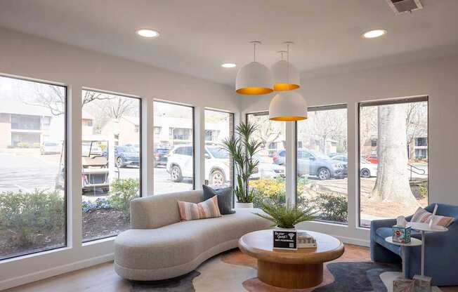 A living room with a grey couch, a wooden coffee table, and a large window with a view of a parking lot.