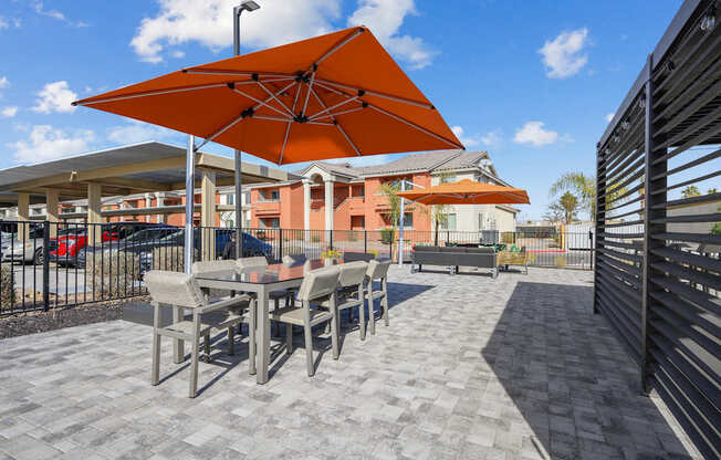 A patio with a table and chairs under an orange umbrella.