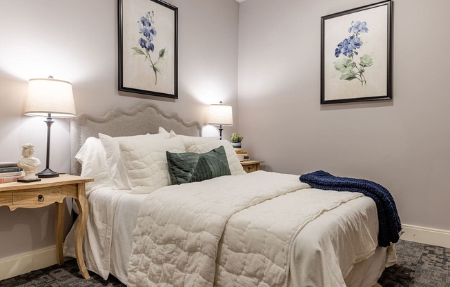 A bedroom with a bed, two lamps, and two framed pictures on the wall.