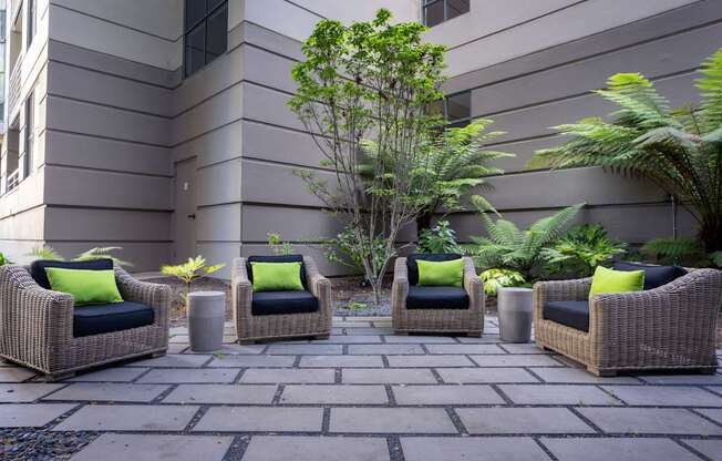 Four wicker chairs with green pillows are arranged on a patio.