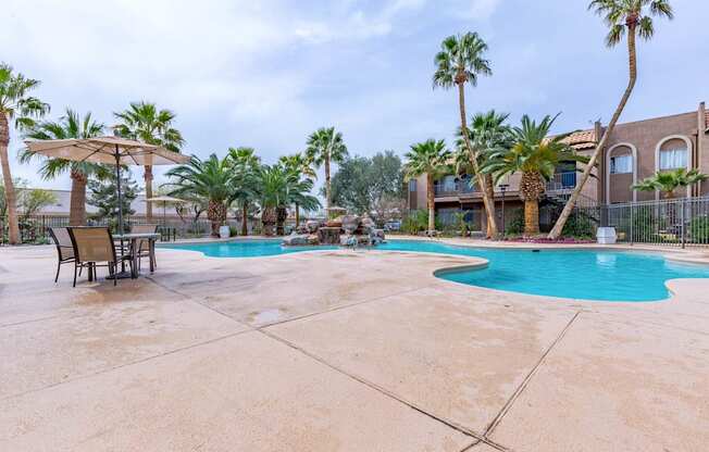 A pool surrounded by palm trees and a building in the background.