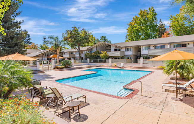 A pool surrounded by chairs and umbrellas with apartment buildings in the background.