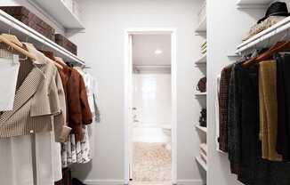 A hallway with a white door and clothes hanging on both sides.