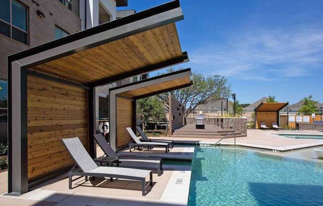 a pool with two lounge chairs next to a building at Hunters Creek Apartments, Texas, 76210