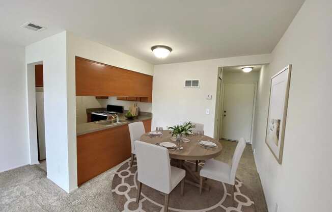 a dining area with a table and chairs and a kitchen in the background at The Landings Apartments, Westland, MI