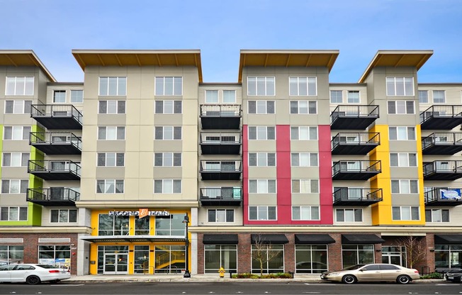 A multi-story apartment building with balconies and a storefront at the ground level.