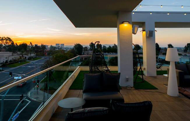A balcony with a table and chairs overlooking a street at sunset.
