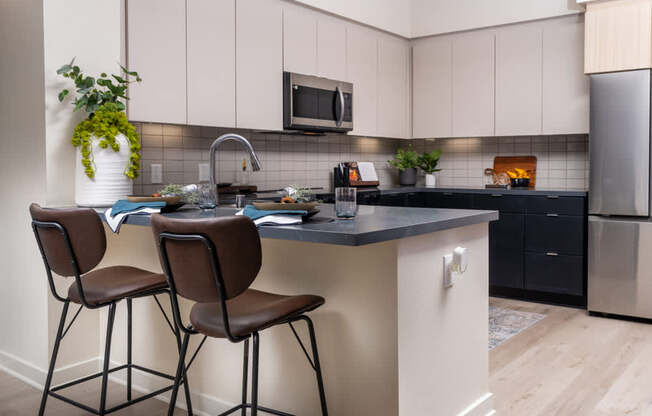 A kitchen with a black countertop and brown chairs.