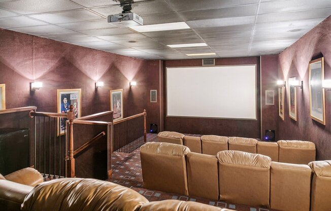 A row of brown leather seats are arranged in front of a large screen in a theater room at Ridge Crossings Apartments, Hoover, AL 35244