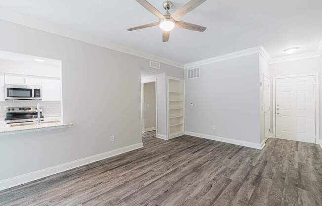 an empty living room with a ceiling fan and a kitchen