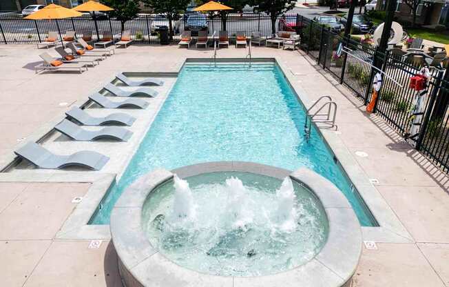 A fountain in the middle of a pool surrounded by lounge chairs.