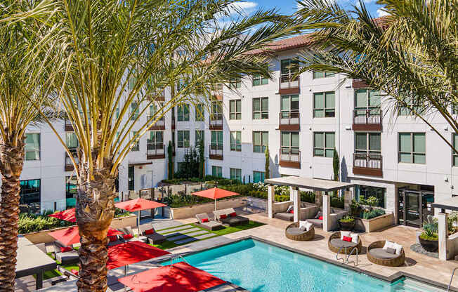 Resort-style pool courtyard with red umbrellas, palm trees, and private cabanas designed for relaxation and connection