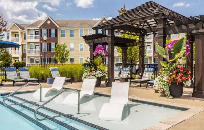 a swimming pool with lounge chairs and a gazebo with an apartment building