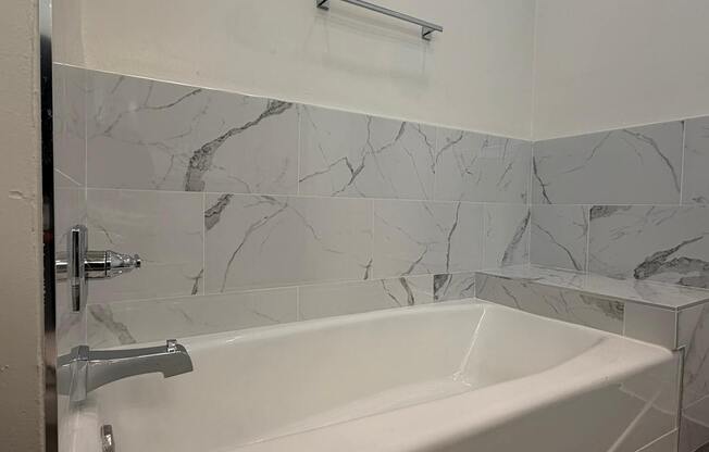 A white bathtub with a silver faucet and a marble tile wall.