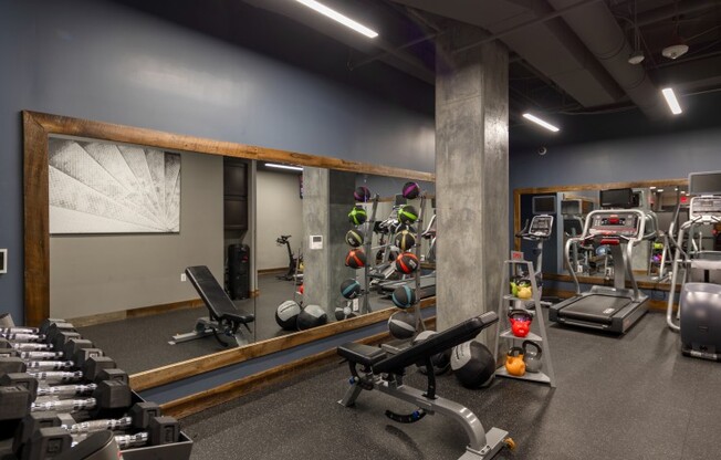 The gym at our apartments for rent in Washington DC, featuring weight balls, a bench press, and free weights.