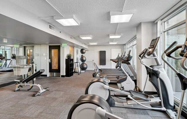a gym with various exercise machines and windows