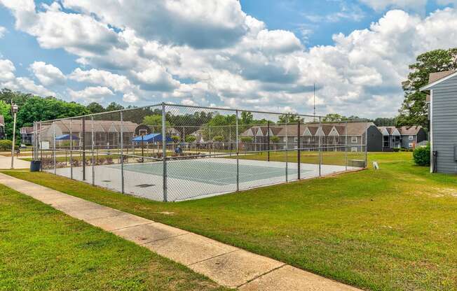 a fenced in tennis court with a volleyball court in front of houses