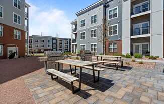 A wooden table and benches are set up in a courtyard with brick pavers.