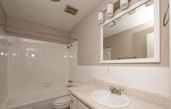 A bathroom with a white toilet, sink, and mirror.