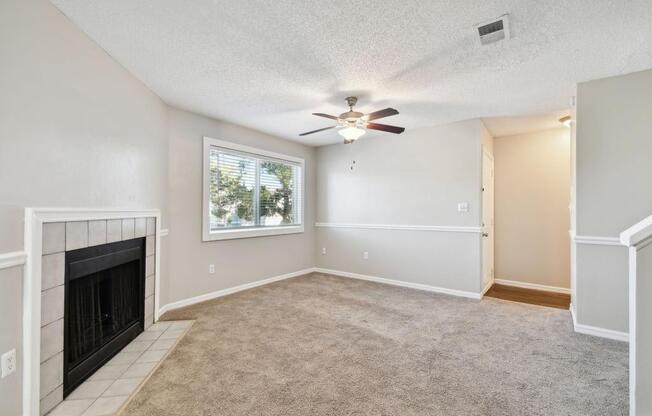 an empty living room with a fireplace and a ceiling fan