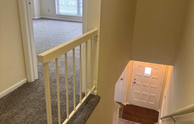 A staircase with a carpeted runner and white balusters leads to a door at the bottom.