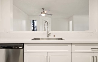 A white kitchen with a stainless steel dishwasher and a silver sink.