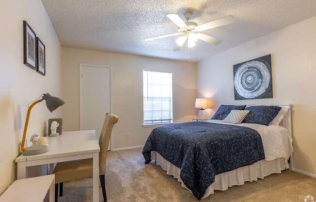 A bedroom with a bed, desk, chair, and window.