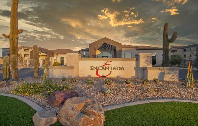 The image shows a building with the word "Encantada" on it, surrounded by cacti and rocks.