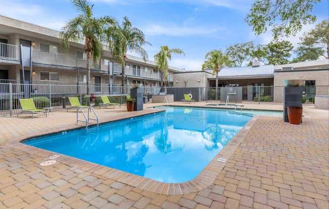 A swimming pool surrounded by a brick patio and palm trees.
