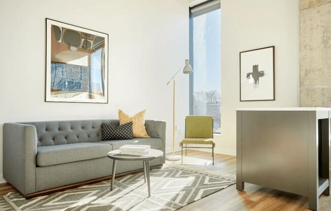 A grey couch with a yellow pillow is in front of a window.