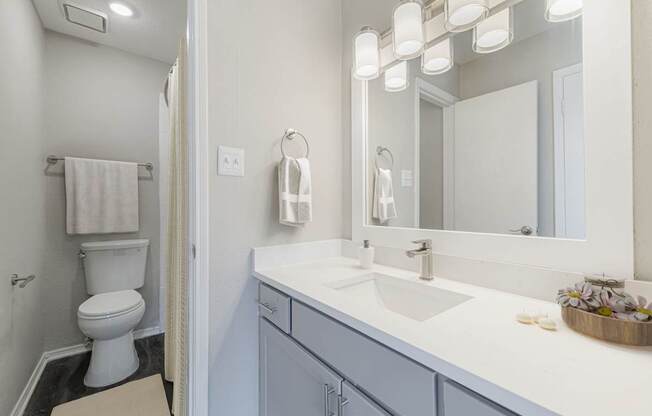 A white toilet is in a bathroom with a white sink and a mirror.
