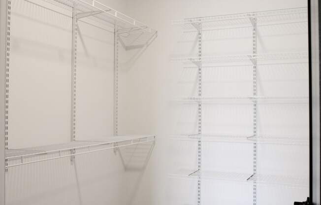 a walk in closet with white shelving and white walls