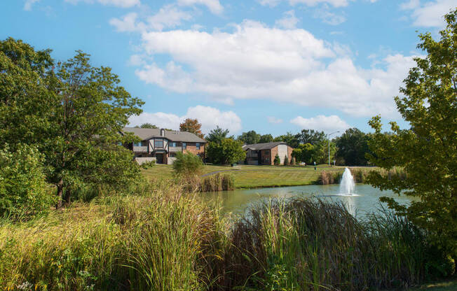 a pond with a fountain and houses in the background