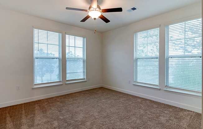 an empty living room with a ceiling fan and three windows
