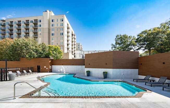 A large swimming pool with lounge chairs and a fence around it.