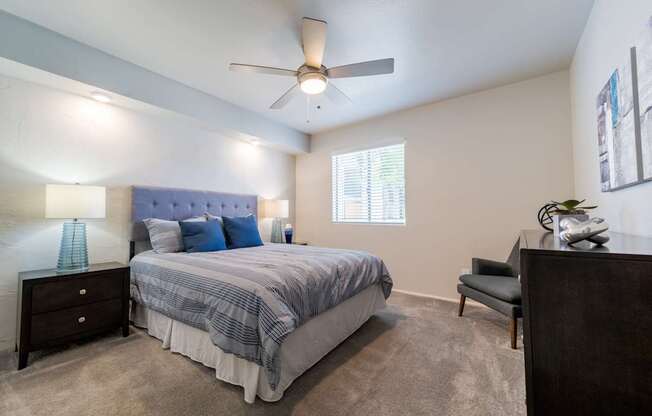 A bedroom with a bed, chair, and ceiling fan.