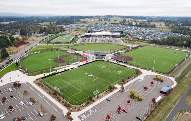 An aerial view of a sports complex with a soccer field, football field, and parking lot.