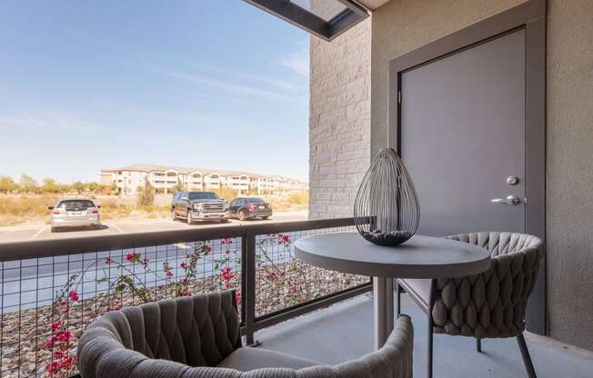 A balcony with a table and two chairs overlooking a parking lot.