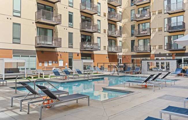 A large outdoor pool area with sun loungers and apartment buildings in the background.