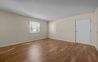 the spacious living room of an empty home with wood flooring and a window