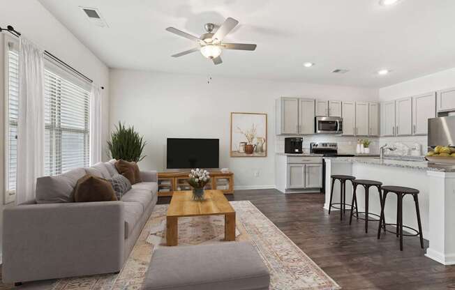 A modern living room with a grey couch, a wooden coffee table, and a kitchen area in the background.