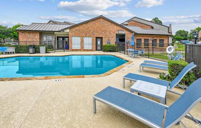 A pool with a blue lounge chair and a brick building in the background.