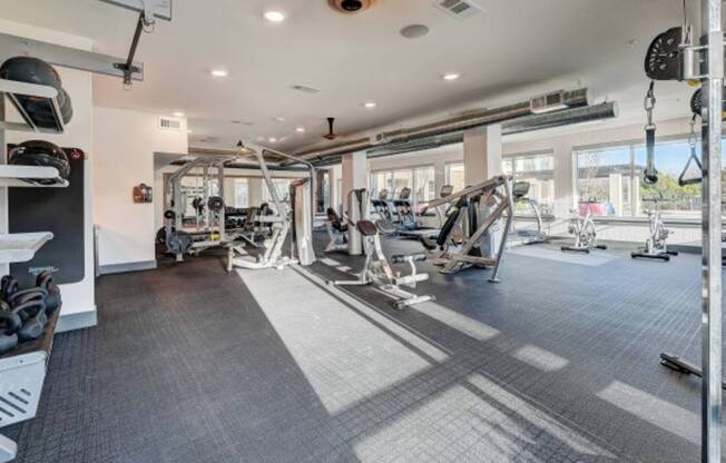 a gym with weights and other equipment in a building with windows at The Jane at Preston Trail, Texas, 75104