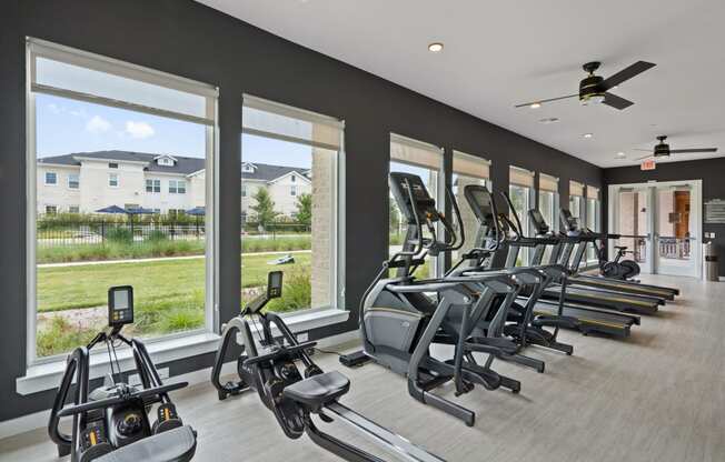 the gym is equipped with a row of cardio machines and windows