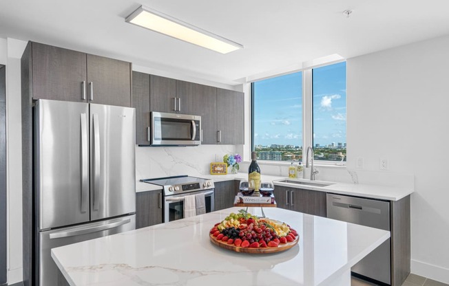 a kitchen with stainless steel appliances and a large island with a fruit centerpiece