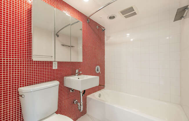 A red tiled bathroom with a white toilet, sink, and bathtub.