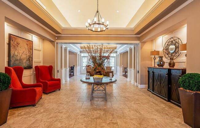 a lobby with red chairs and a table and a chandelier